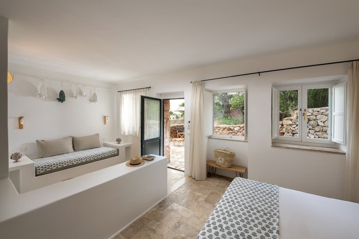 Un dormitorio moderno con una banca integrada, una cama con ropa de cama estampada, una mesita y vistas al exterior.
