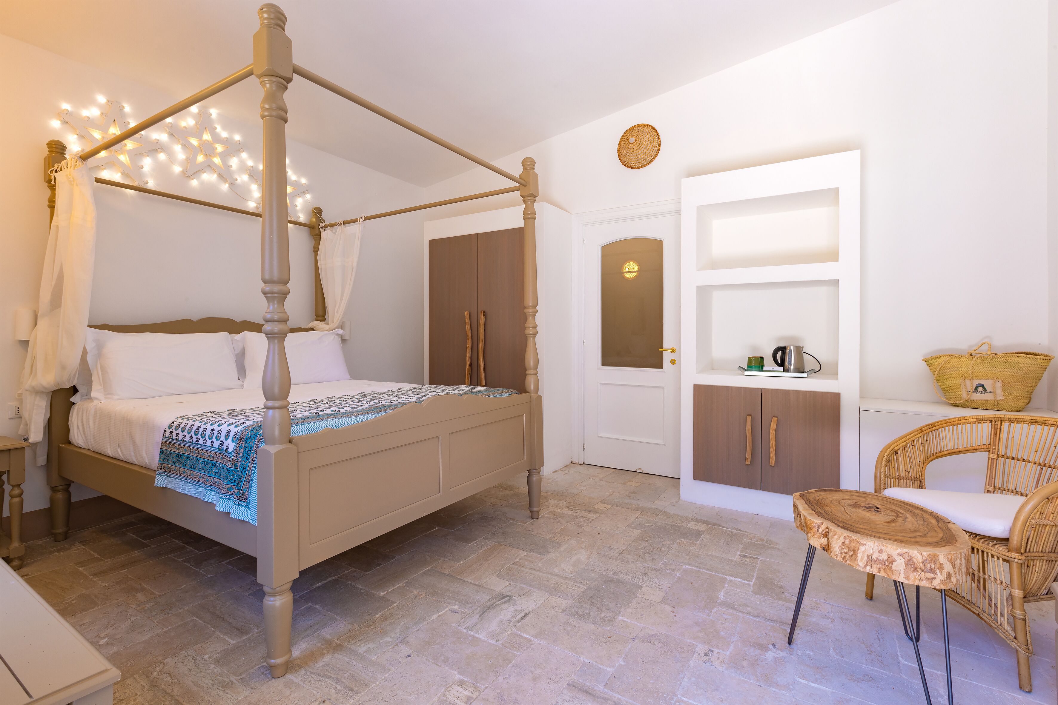 Una camera da letto con un letto a baldacchino, una sedia in vimini e un armadio bianco.