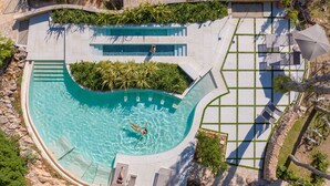 Ein Schwimmbecken mit geschwungenem Design, umgeben von Liegestühlen und einem gepflasterten Weg.