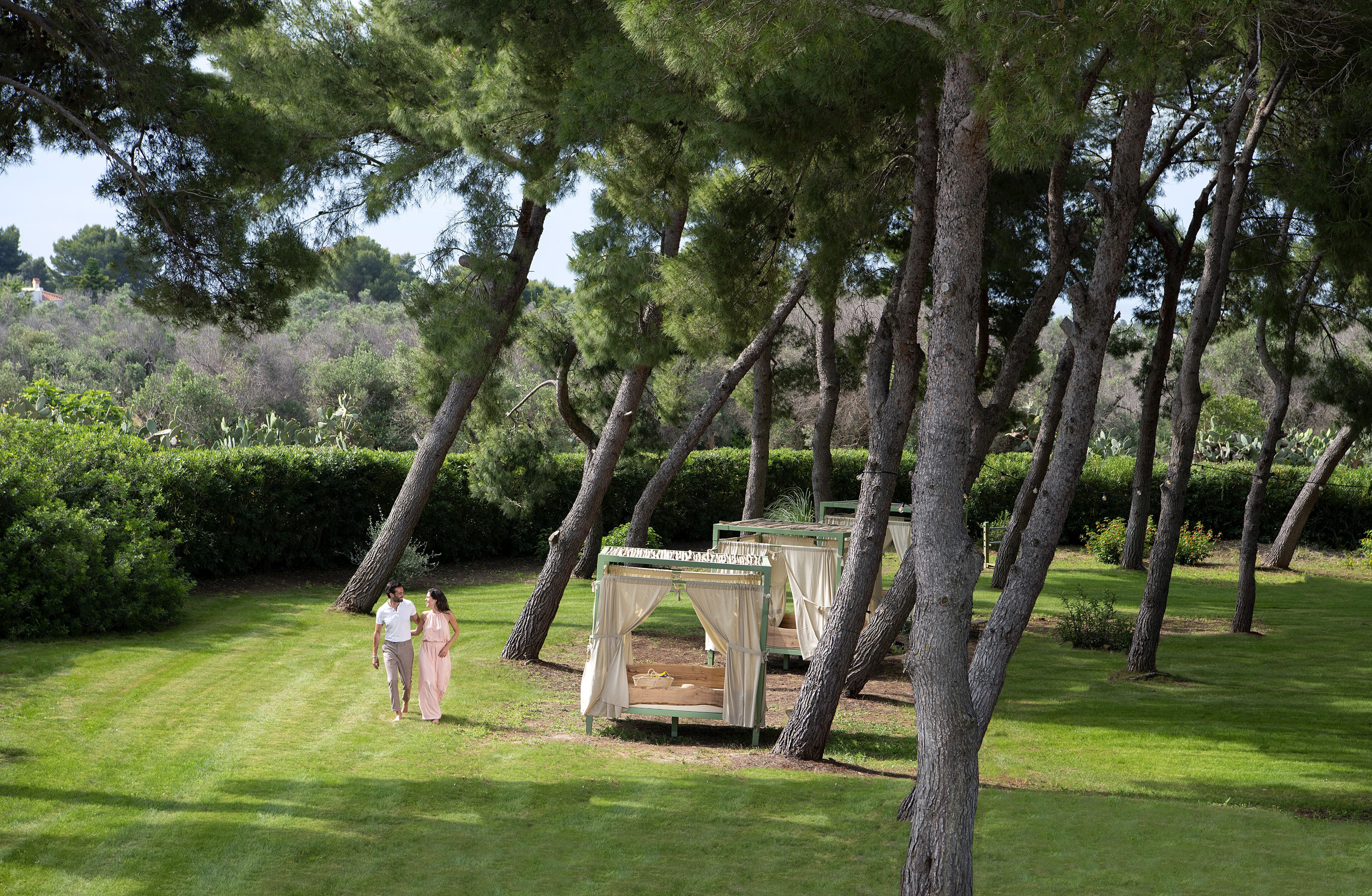 A grassy outdoor area with several tree-lined beds and a couple walking.
