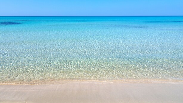 Ein klarer Blick auf einen Strand mit sandigem Ufer und ruhigem türkisfarbenen Wasser.