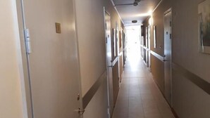 A long, narrow hotel corridor with doors on both sides, a tiled floor, and a ceiling light fixture. - Motoristen (Vara)