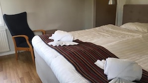 A neatly made bed with white linens and a striped blanket, a wooden chair, and a bedside table with a lamp. - Motoristen (Vara)
