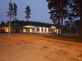 Um motel com estrutura em um único pavimento, área de estacionamento coberta e placa indicando sua finalidade.
