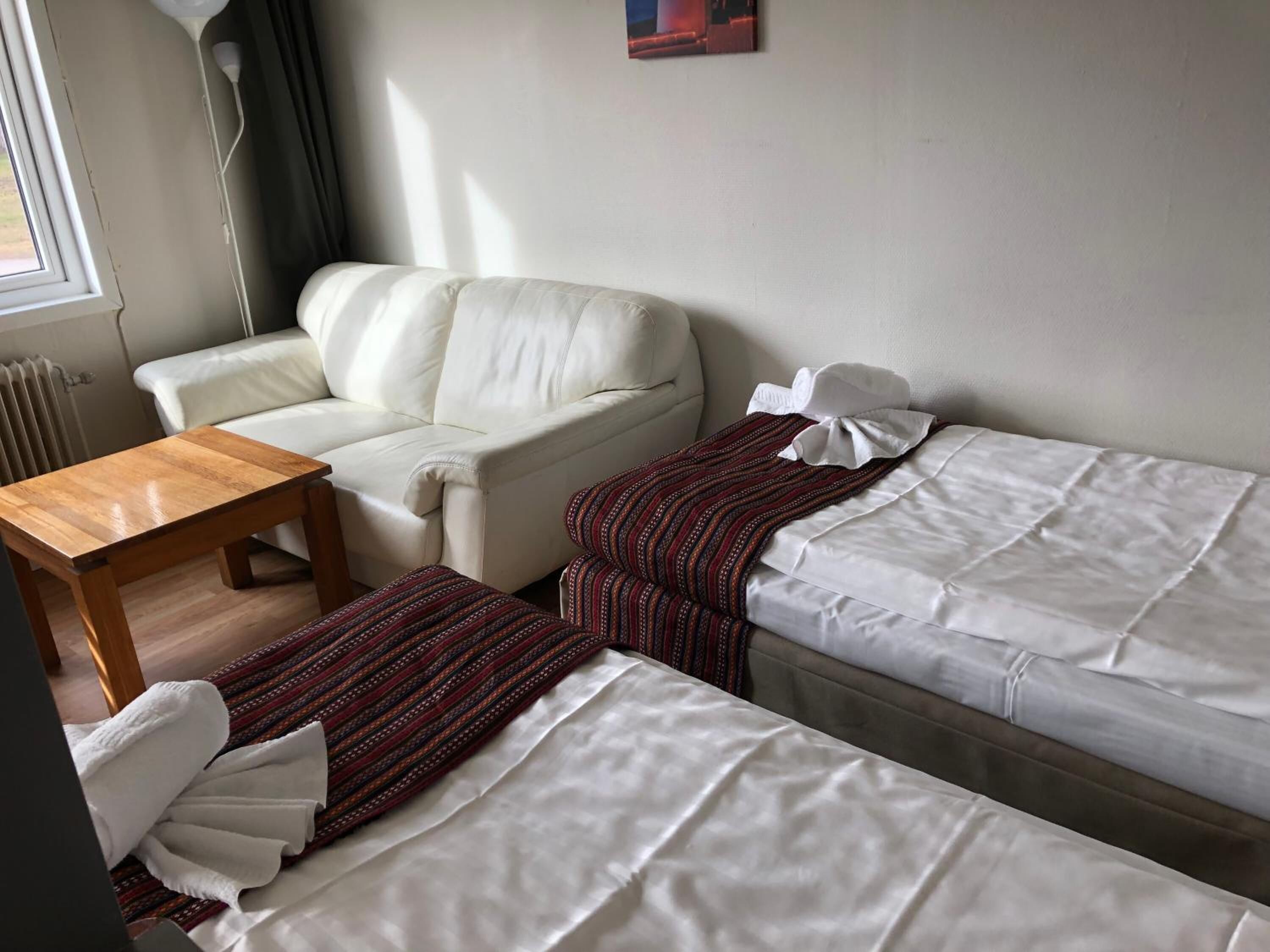 Una habitación con un sofá blanco, una mesa de madera y una cama con ropa blanca.
