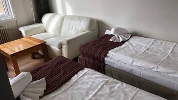 Una habitación con un sofá blanco, una mesa de madera y una cama con ropa blanca.