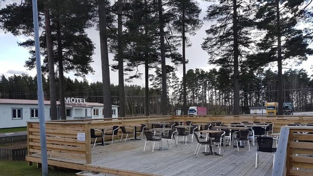 A motel with outdoor seating area, surrounded by tall trees. - Motoristen (Vara)