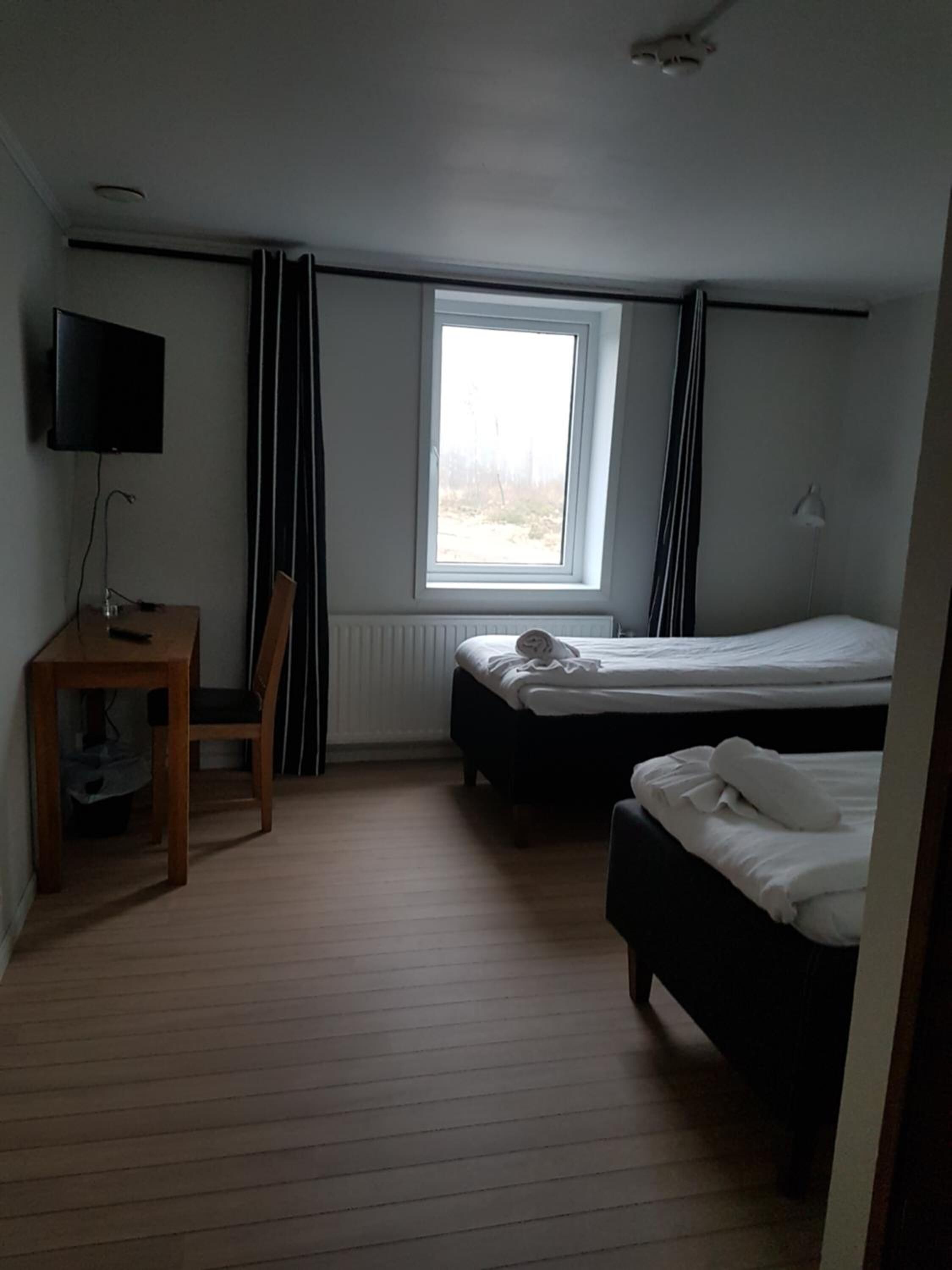 A hotel room with a single bed, a desk with a computer, a TV, and a window with curtains.