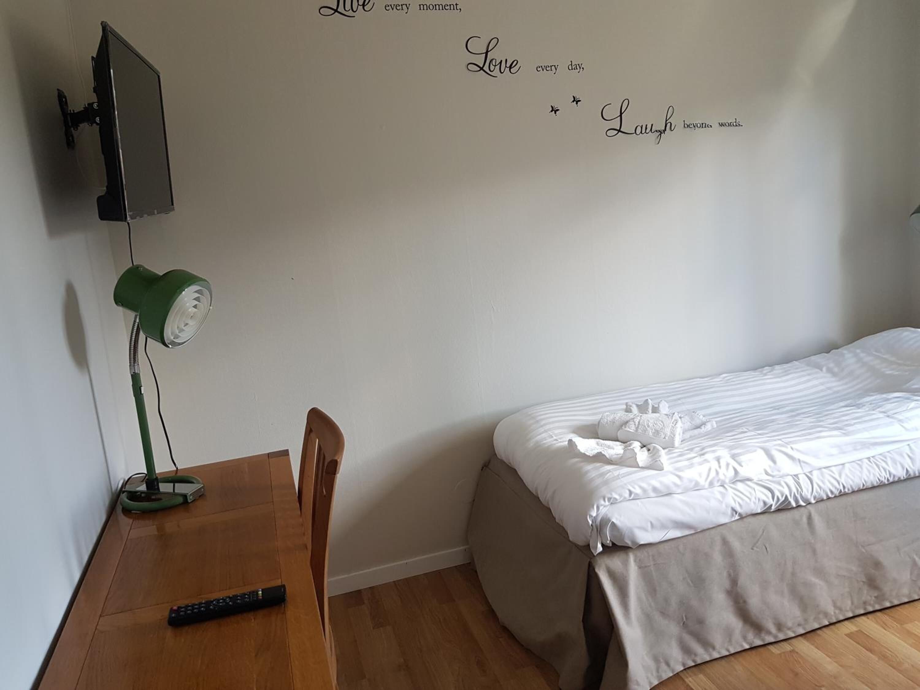 Ett sovrum med en säng, ett skrivbord med en lampa, en tv som är monterad på väggen och en vägg med inspirerande citat.