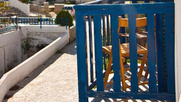 A terrace with a blue railing, a wooden chair, and a view of white buildings with blue domes in the background. - Angelos Rooms (Naxos)