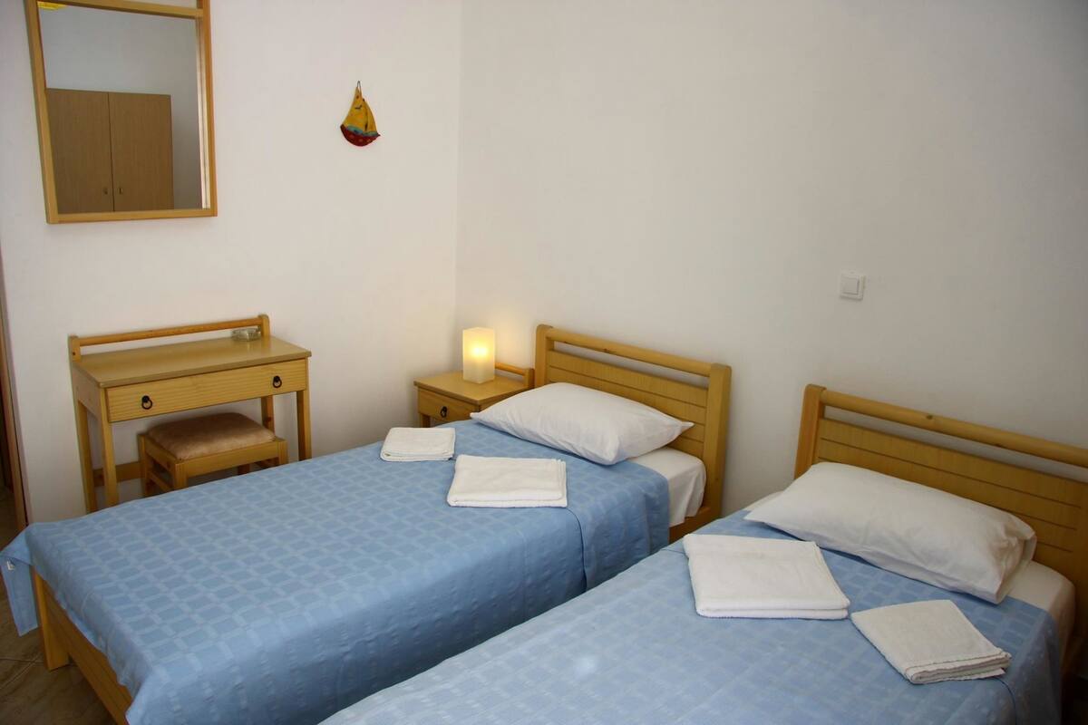A bedroom with two beds, a desk, and a nightstand with a lamp.