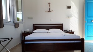 A neatly made bed with white linens, a wooden headboard, and a nightstand with a lamp. - Angelos Rooms (Naxos)