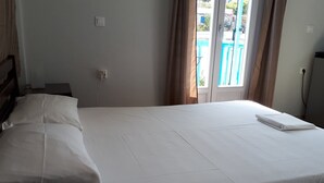A neatly made bed in a room with a view of a swimming pool through a glass door. - Angelos Rooms (Naxos)