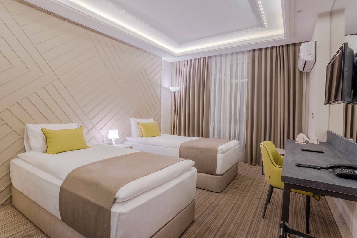 A hotel room with two beds, a desk, a chair, a TV, and an air conditioning unit.