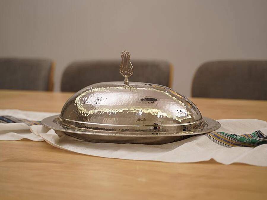 A covered food service item on a table with a white cloth underneath.