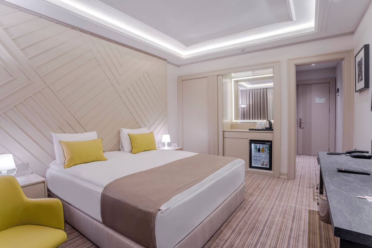 A hotel room with a bed, bedside table, lamp, and a small refrigerator.