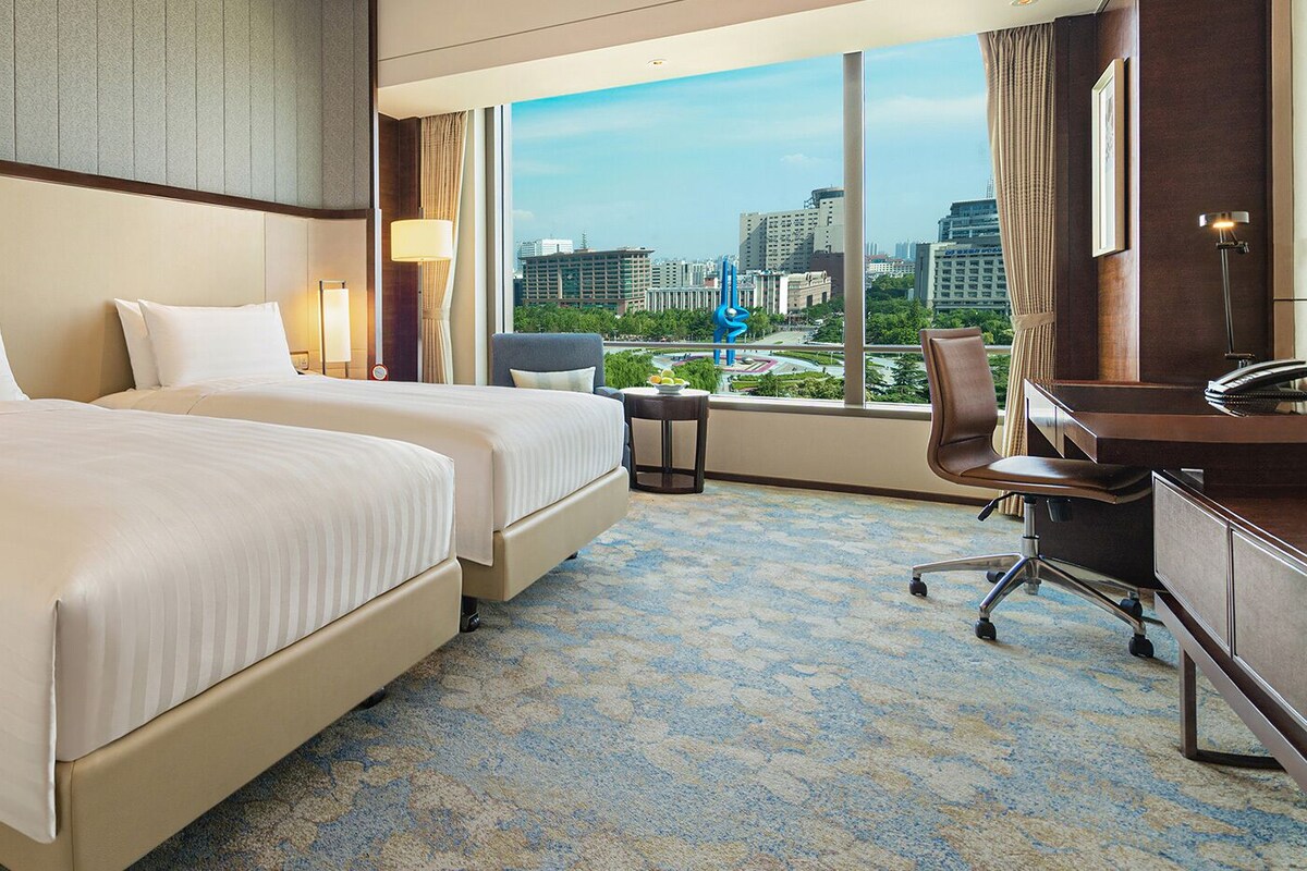 Habitación de hotel con dos camas, un escritorio, una silla y vista a la ciudad.