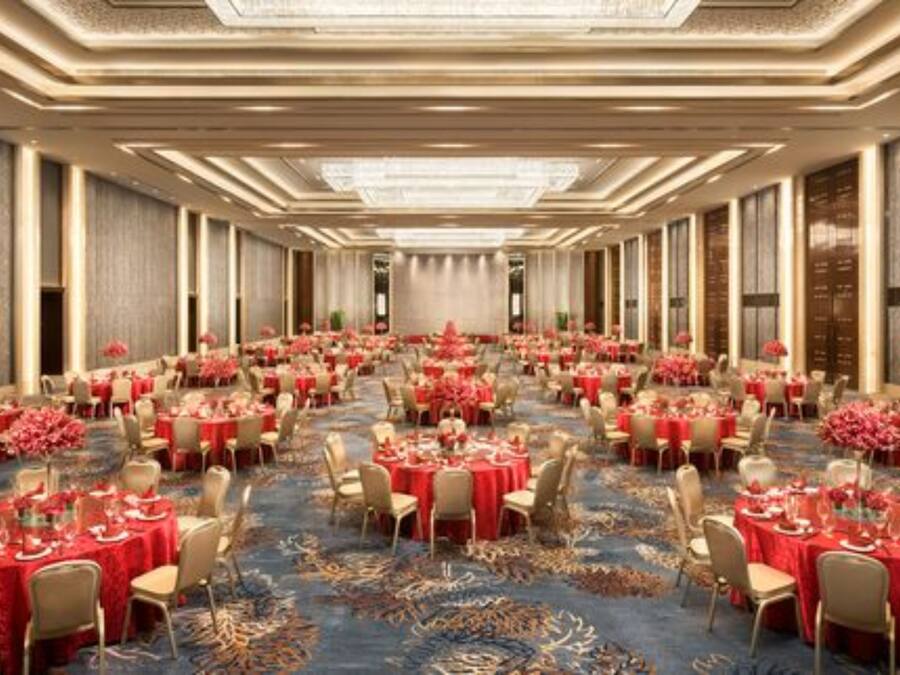 A large banquet hall with multiple round tables covered in red tablecloths, arranged in rows.