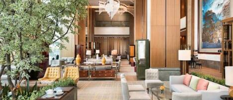 A spacious lobby with a large tree, comfortable seating, and a modern chandelier.