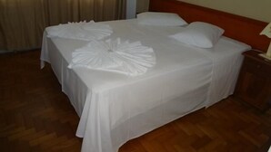 A neatly made bed with white linens and decorative pillows, a wooden headboard, and a wooden floor. - Grande Hotel Torres (Torres)