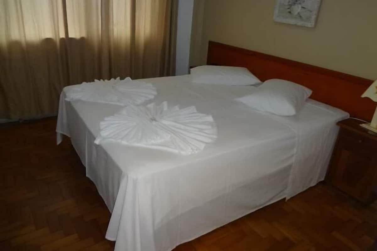 A neatly made bed with white linens and decorative pillows, a wooden headboard, and a wooden floor.