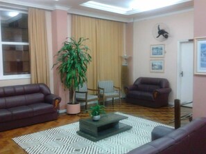 Ein Wohnzimmer mit zwei Ledersofas, einem Couchtisch, einer Zimmerpflanze, einem gemusterten Teppich und einem großen Fenster mit Vorhängen.