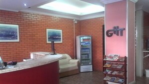 A reception area with a red counter, a vending machine, a couch, and a wall with a large 'G' sign. - Grande Hotel Torres (Torres)