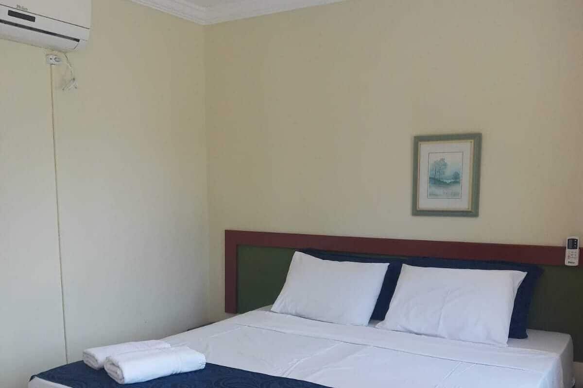 Une chambre d’hôtel avec un grand lit, un climatiseur fixé au mur et un tableau encadré accroché au mur.