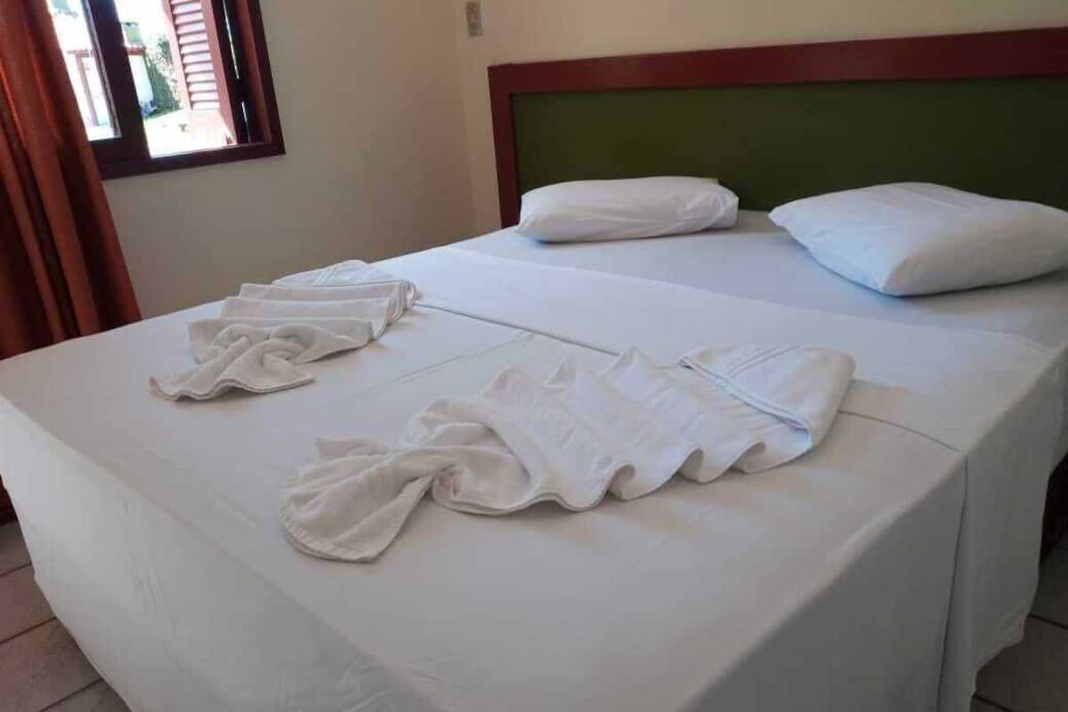 Un lit bien fait, avec du linge de lit blanc et des oreillers, une tête de lit verte et une fenêtre avec des rideaux.