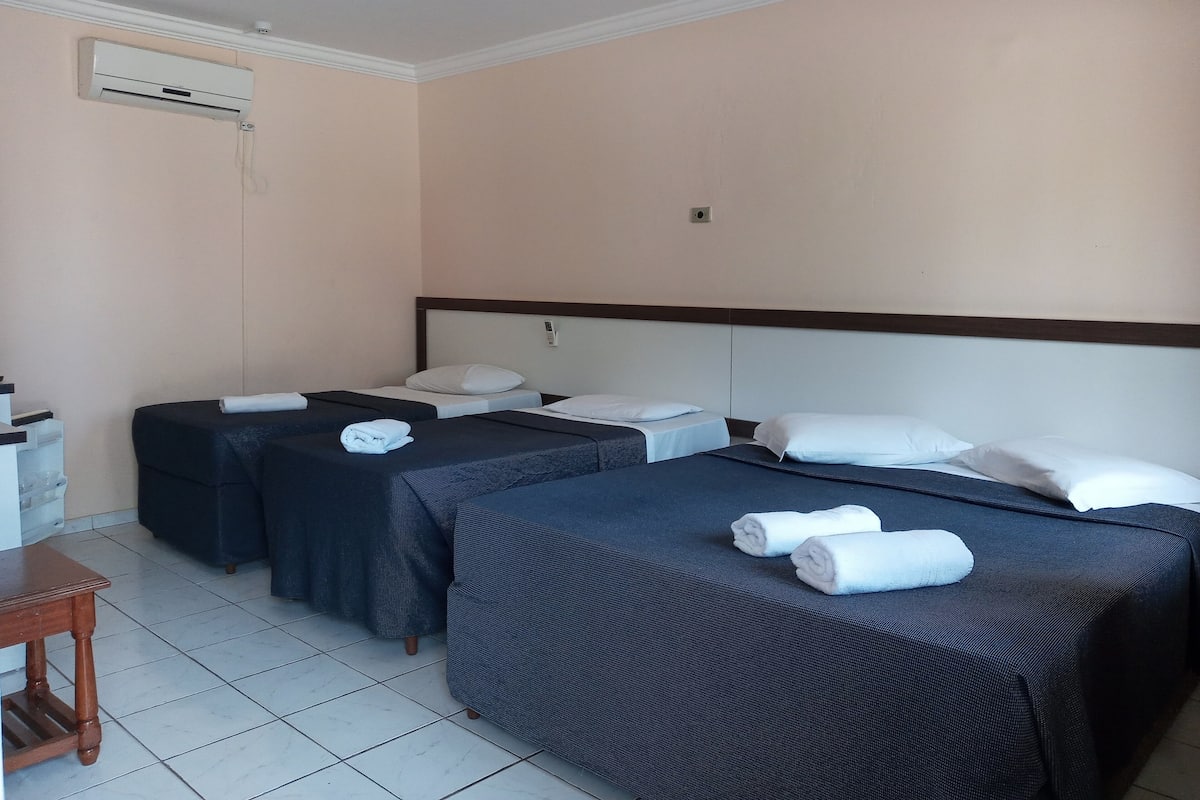 Une chambre d’hôtel avec deux lits simples, une table en bois et un appareil de climatisation fixé au mur.