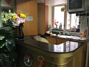 A reception desk with a 'No Smoking Area' sign, a vase of flowers, and various items on the counter. - Tohou Hotel (Kowloon)