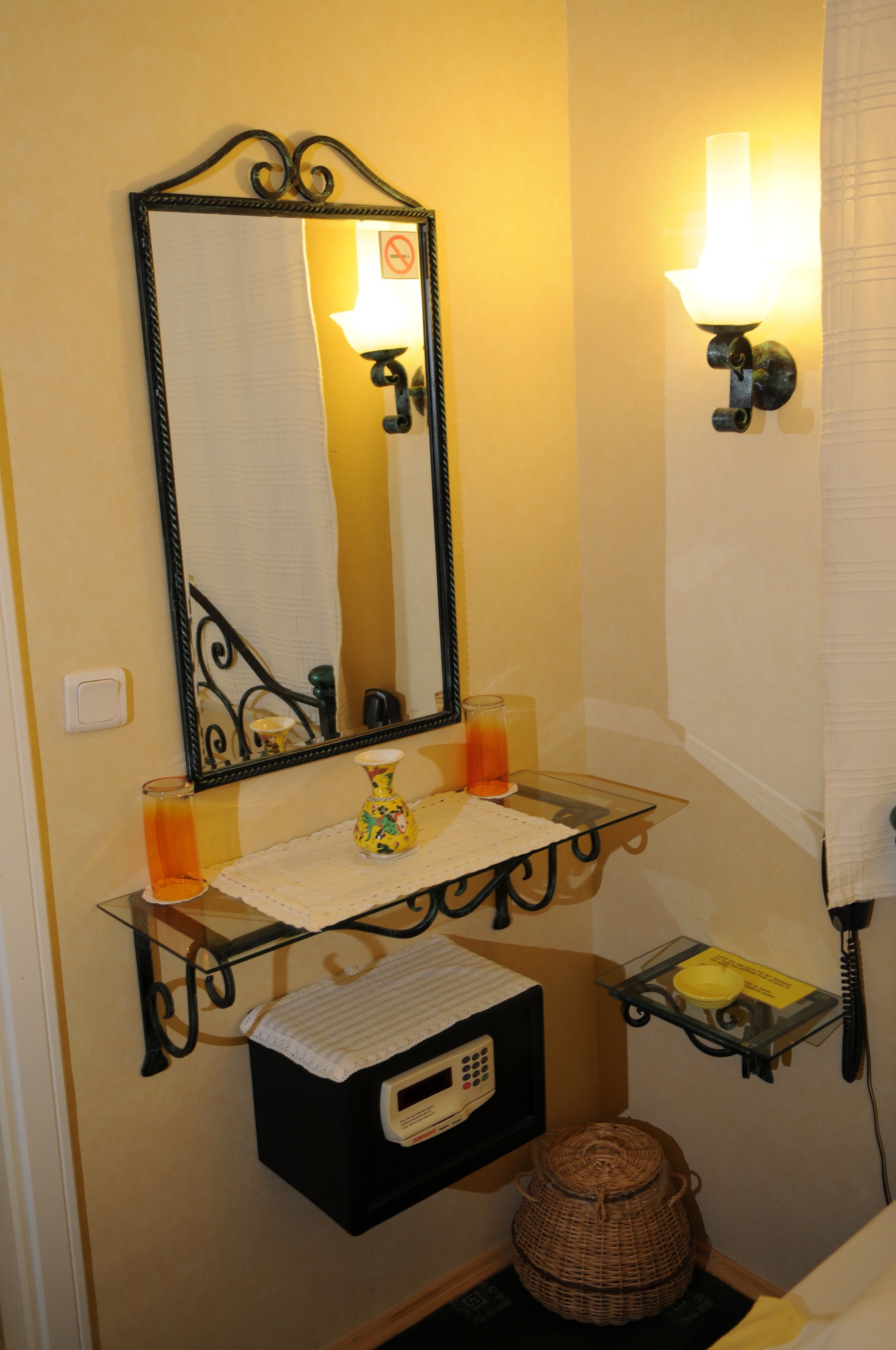 A bathroom with a mirror, a sink, a vase, a telephone, and a basket.