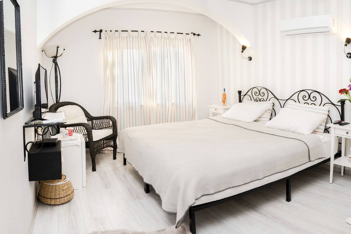 A bedroom with a large bed, a chair, a nightstand, a lamp, and a mirror.