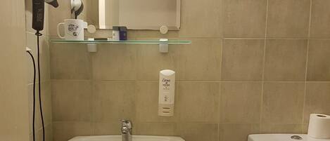 A bathroom with a sink, toilet, and a hairdryer on a wall-mounted shelf.