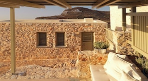 A stone building with two windows, a small door, and a covered outdoor seating area. - Themonies Luxury Suites (Folegandros)