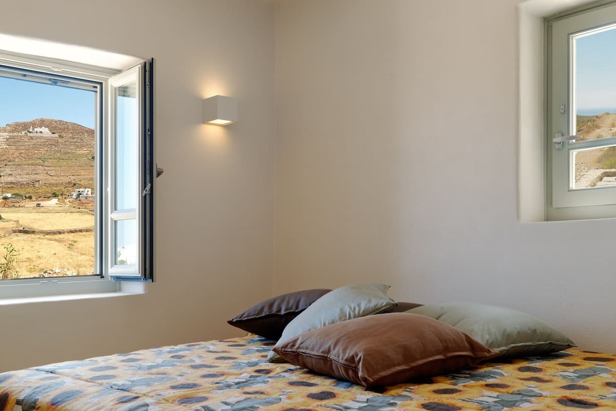A bedroom with a bed, a window, and a view of a hill.