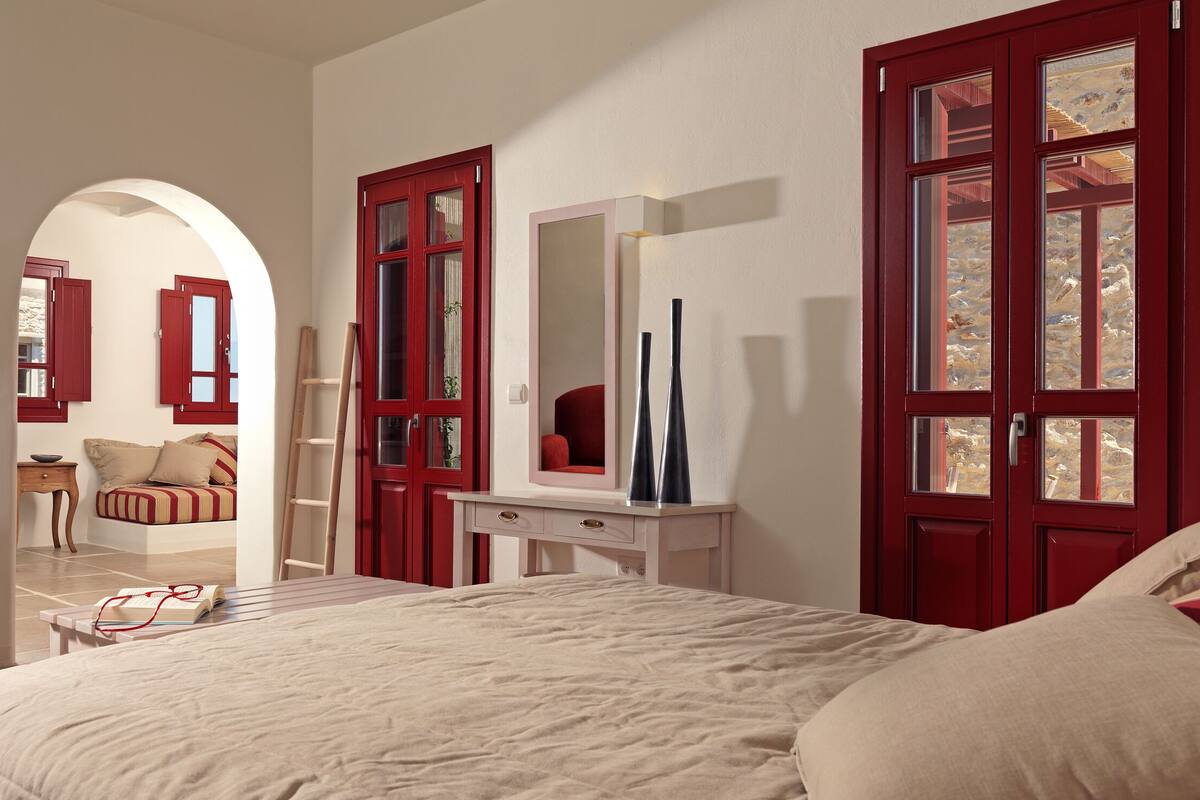 A bedroom with a bed, a red armchair, a dresser, a mirror, and a door with glass panels.