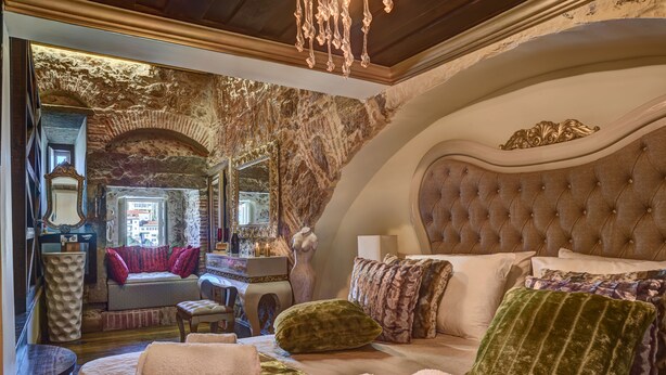 Um quarto luxuoso com uma cama grande, uma penteadeira e vista da cidade através de uma janela em arco.