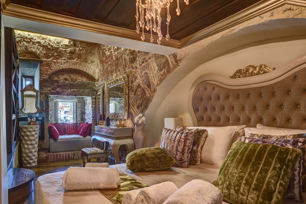 Ein luxuriöses Schlafzimmer mit einem großen Bett, einem Schminktisch und Blick auf die Stadt durch ein rundes Fenster.