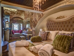 Ein luxuriöses Schlafzimmer mit einem großen Bett, einem Schminktisch und Blick auf die Stadt durch ein rundes Fenster.