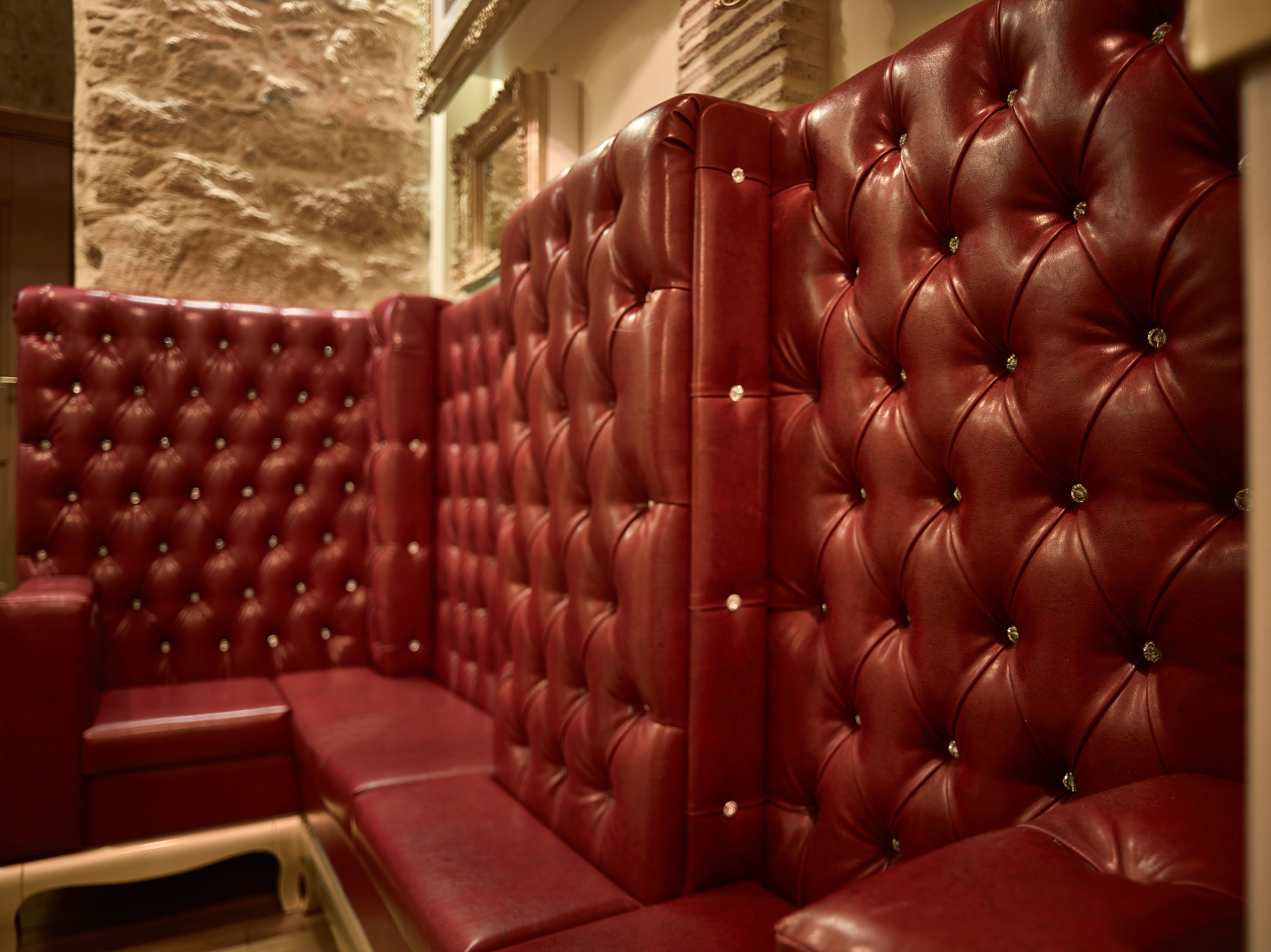 A section of a red leather booth with a tufted backrest and armrests, set against a stone wall.