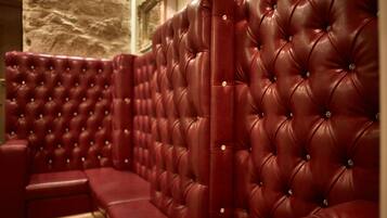 A section of a red leather booth with a tufted backrest and armrests, set against a stone wall.