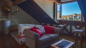 Um quarto acolhedor com teto inclinado, uma banheira, um sofá com almofadas vermelhas e vista para a cidade através de uma janela grande.