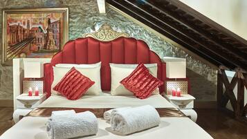 A bedroom with a large bed, red headboard, white nightstands, and a painting on the wall.