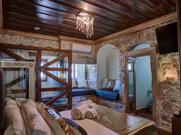 A room with a stone wall, wooden ceiling, a bed with towels, a bench, and a chandelier. - Solar Antigo Luxury Coimbra (Coimbra)