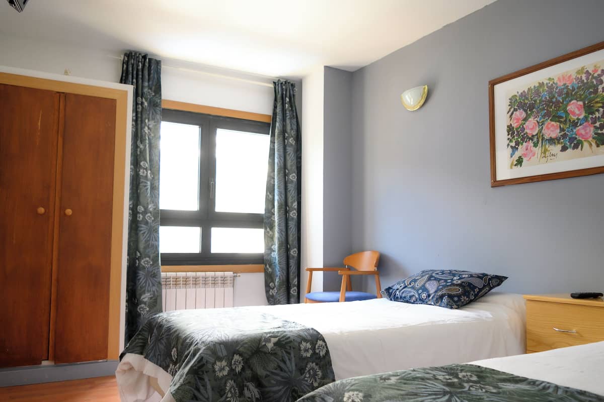 Een slaapkamer met twee bedden, een houten garderobe, een stoel, een nachtkastje en een raam met gordijnen.