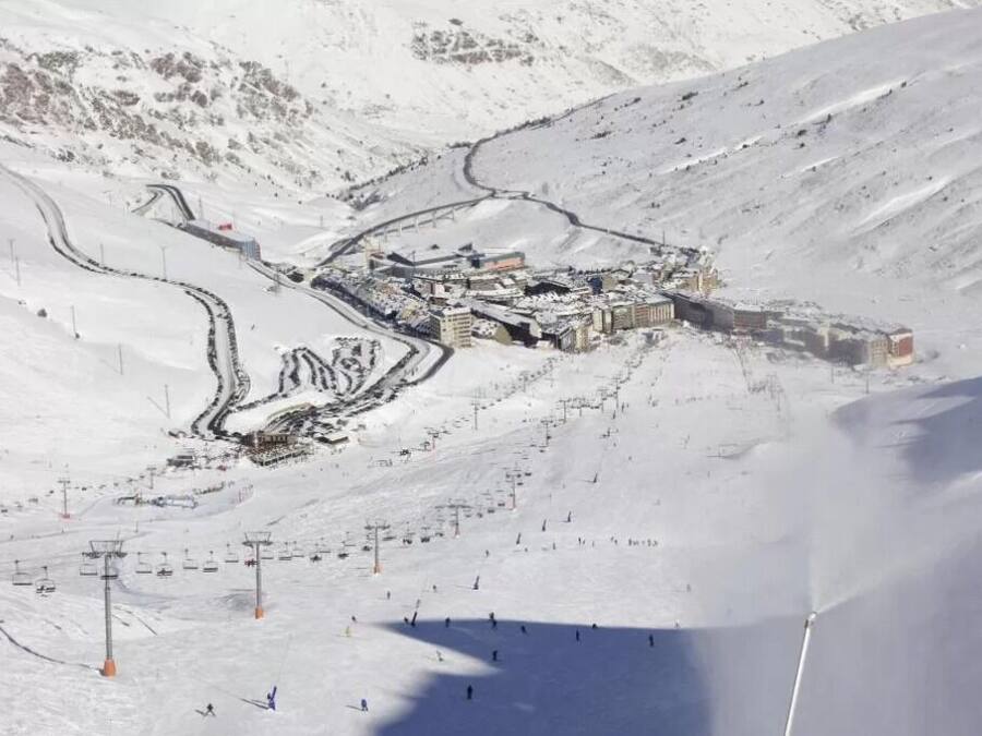 Estación de esquí nevada con remontes, una cabaña y montañas al fondo.