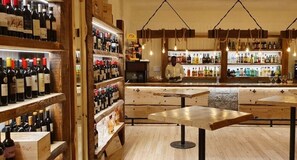 Un bar avec des étagères en bois remplies de bouteilles, un comptoir et des luminaires suspendus.