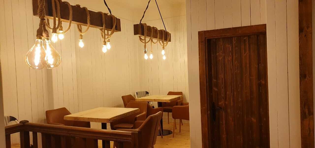 A dining area with wooden tables and chairs, hanging light fixtures, and a wooden door.