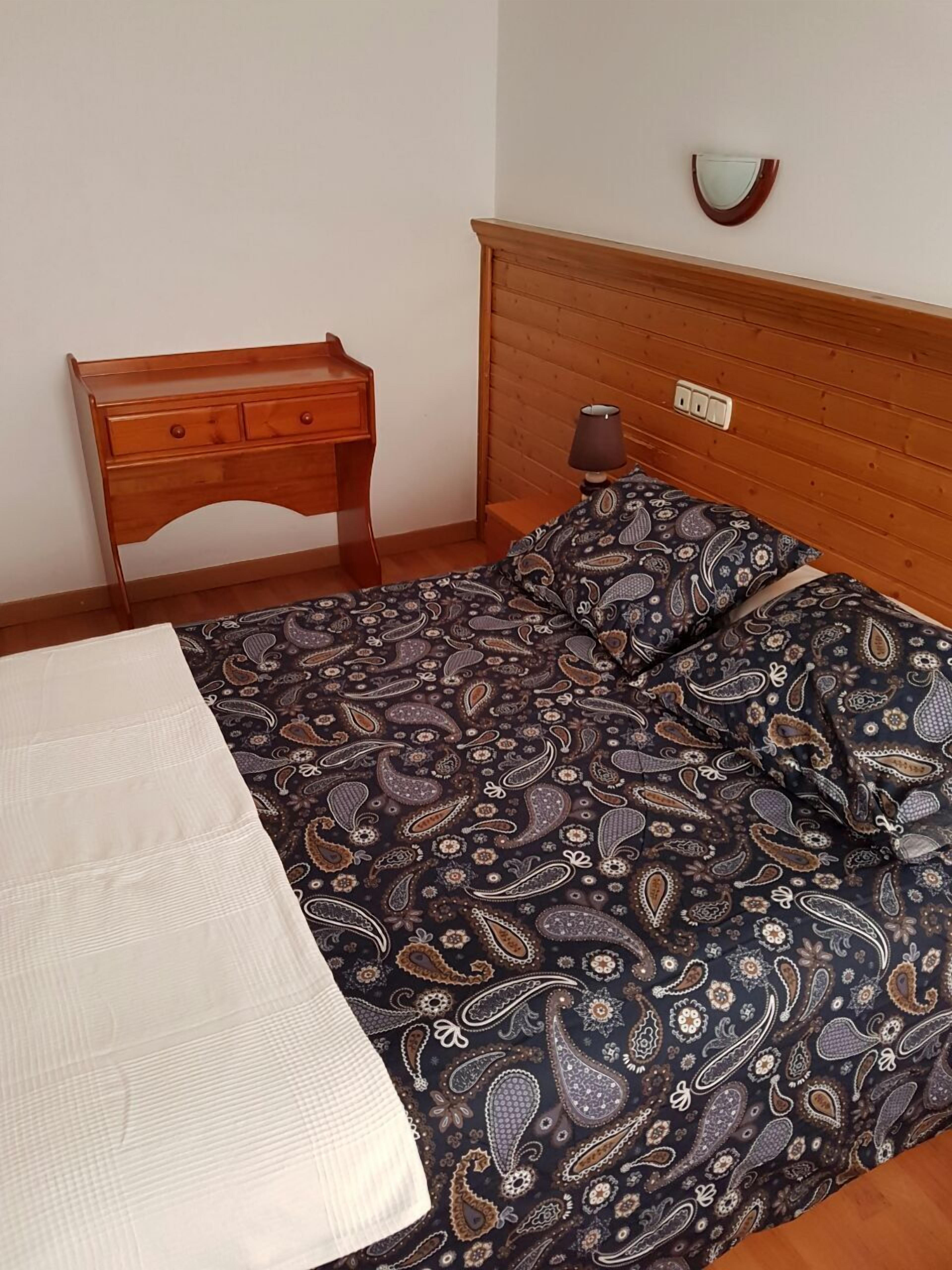 A bedroom with a wooden bed, a nightstand, and a wall-mounted lamp.